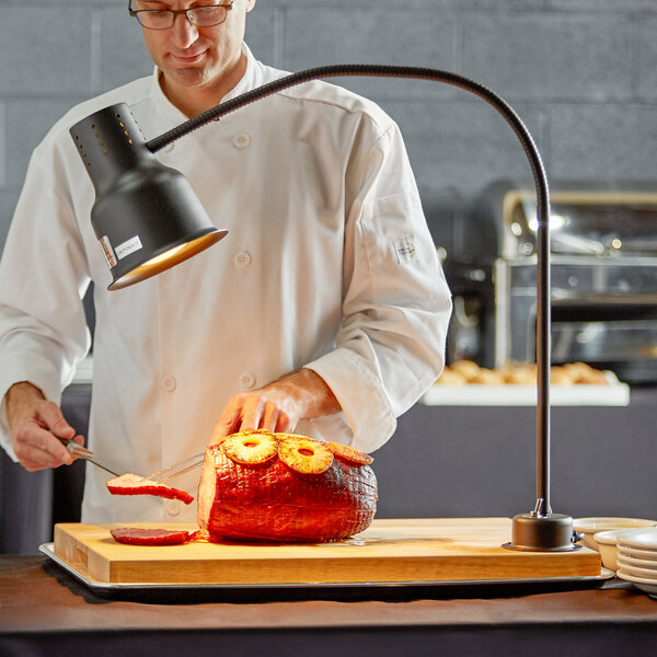 An Avantco carving station with a chef in a white coat cutting a ham on a cutting board.