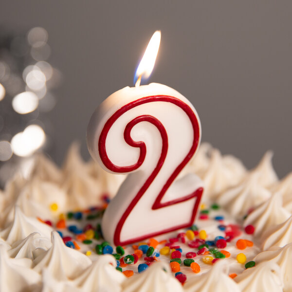 A red and white outlined number two birthday candle on a cake.