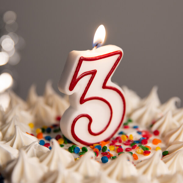 A white and red outlined number three candle on a cake.