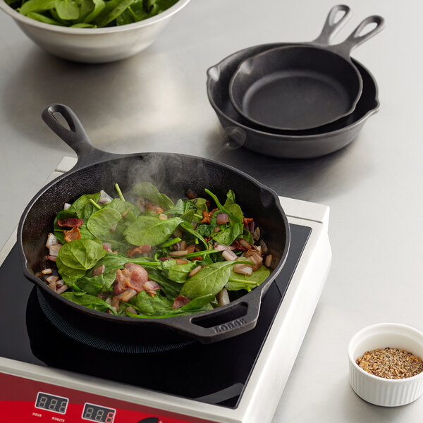 A Lodge cast-iron skillet with spinach and bacon in it on a kitchen counter.