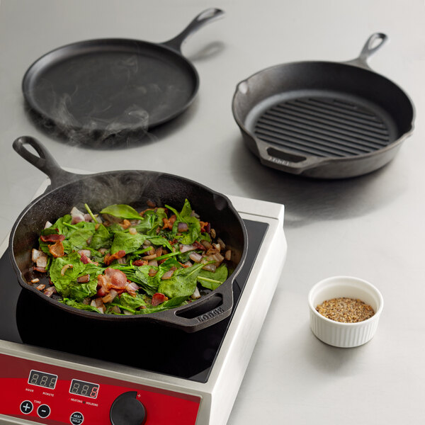 A Lodge cast iron skillet with vegetables and a pan on top of it on a stove.