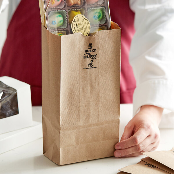 A person holding a Duro brown paper bag full of food.