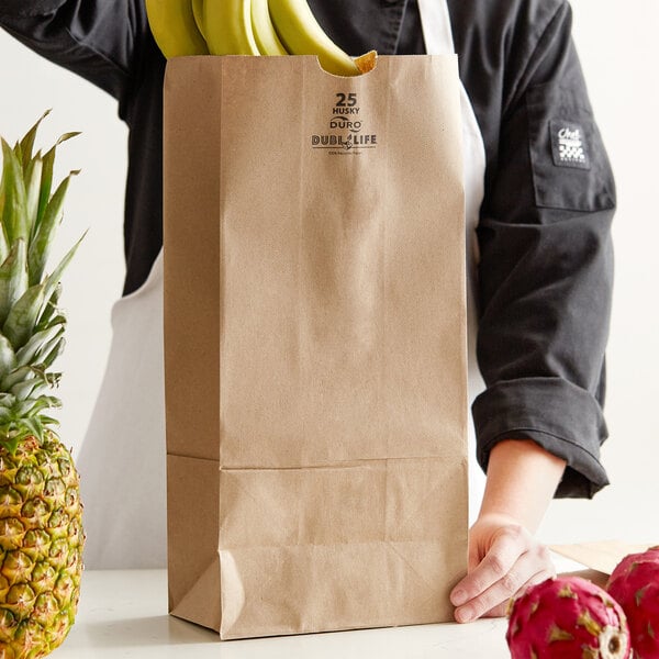 A person holding a Duro brown paper bag full of bananas.