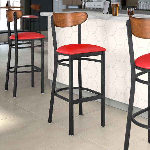 Three Lancaster Table & Seating Boomerang Series black bar stools with red vinyl seats at a restaurant bar counter.