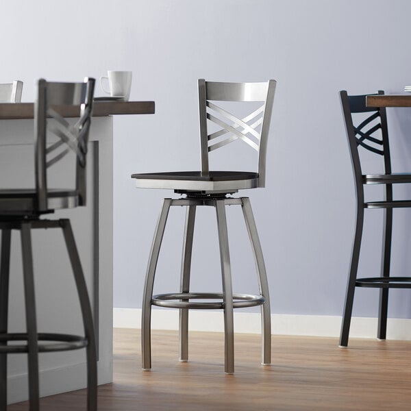 A Lancaster Table & Seating swivel bar stool with a black wood seat at a table in a restaurant.