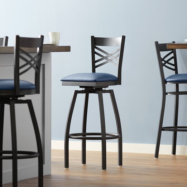 A Lancaster Table & Seating black swivel bar stool with a navy cushion.