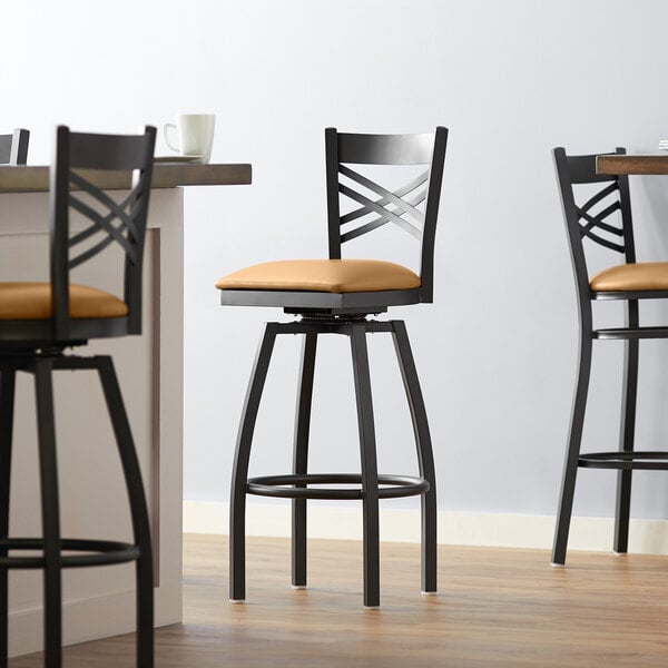 A group of three Lancaster Table & Seating black swivel bar stools with light brown vinyl padded seats at a table.