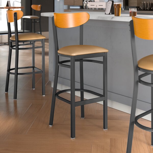Lancaster Table & Seating Boomerang Series bar stools with light brown vinyl seats and cherry wood backs at a restaurant counter.