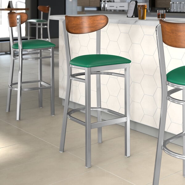 A group of Lancaster Table & Seating bar stools with green vinyl seats and antique walnut backs at a counter.