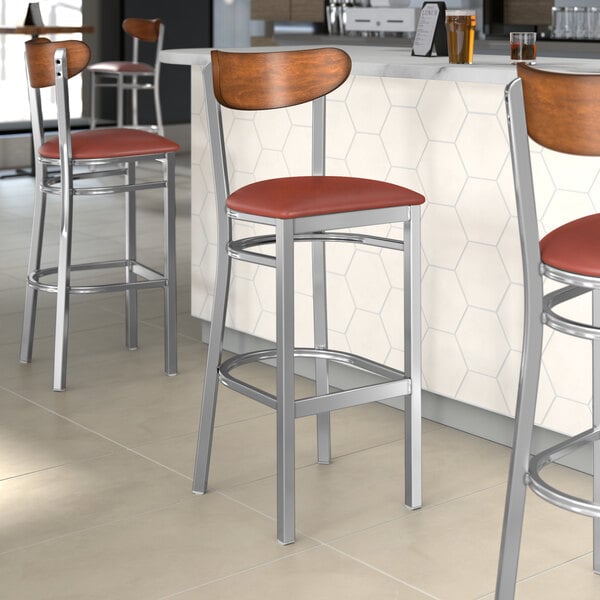 Lancaster Table & Seating Boomerang Series bar stools with a burgundy seat cushion and wood back.