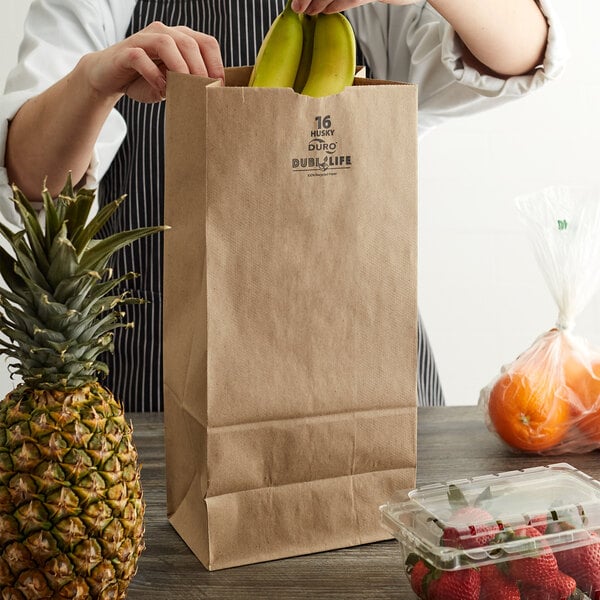 A person holding a Duro brown paper bag with bananas inside.