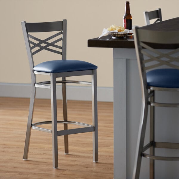 A Lancaster Table & Seating clear coat finish cross back bar stool with a navy vinyl padded seat.