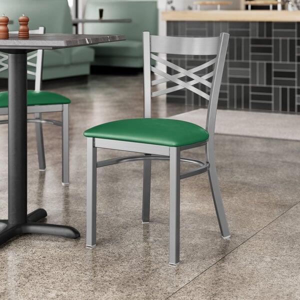 A Lancaster Table & Seating clear coat finish cross back chair with a green vinyl padded seat on a table in a restaurant dining area.