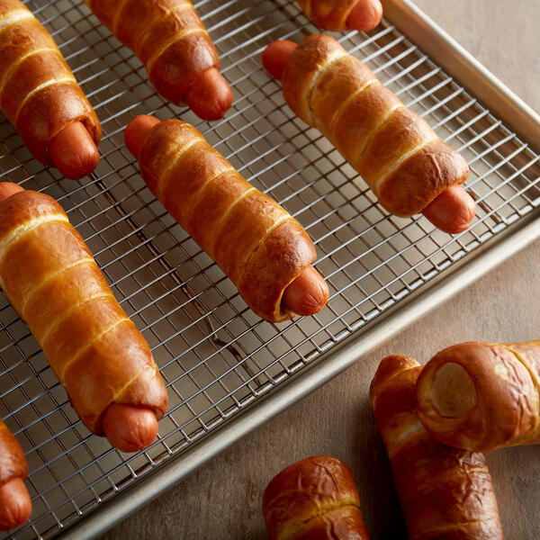 A close-up of hot dogs wrapped in soft pretzel dough on a cooling rack.