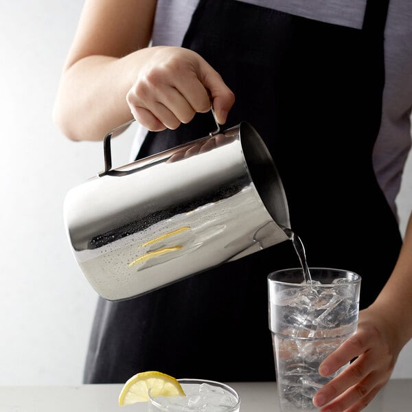 A woman using an Acopa stainless steel pitcher to pour water into a glass.