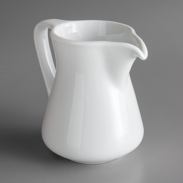 A Oneida Royale bright white porcelain creamer on a gray surface.