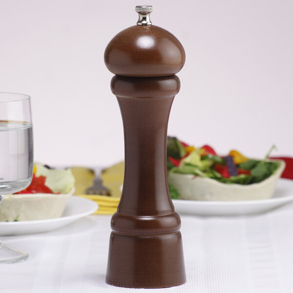 A Chef Specialties Windsor Walnut pepper mill on a table next to a plate of food.