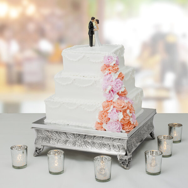 A Tabletop Classics by Walco nickel-plated square cake stand holding a wedding cake with a couple figurines on top.