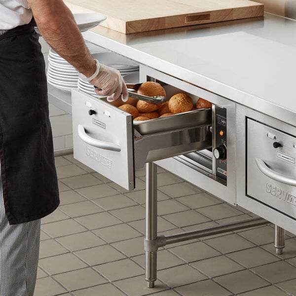 A man using a ServIt double drawer warmer to store food on a counter.