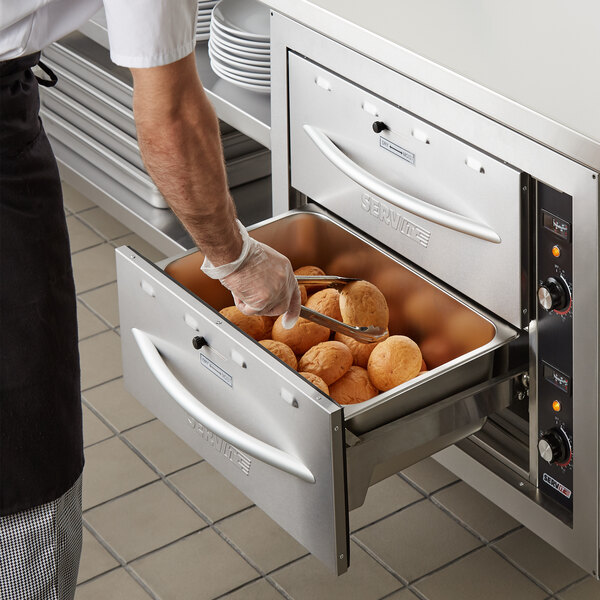 A man using a ServIt double drawer warmer to put bread in a metal container.