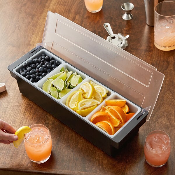 A person holding a Tablecraft 4-compartment condiment bar with sliced lemons, limes, oranges, and berries.