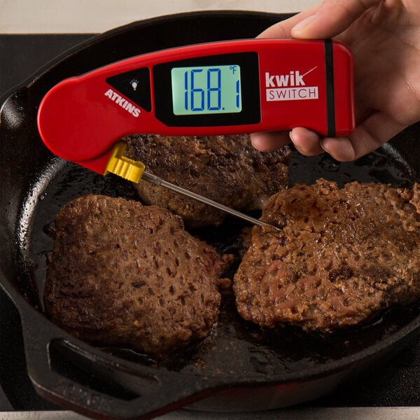 A hand using a Cooper-Atkins red digital thermometer to check the temperature of frying meat.