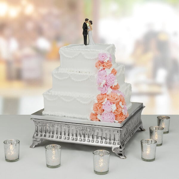 A Tabletop Classics by Walco contemporary square nickel-plated cake stand holding a wedding cake with a couple figurines on top.