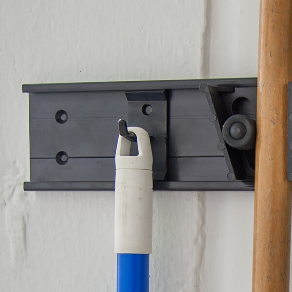 A white broom attached to a wall using a Carlisle Roll 'N Grip hook.