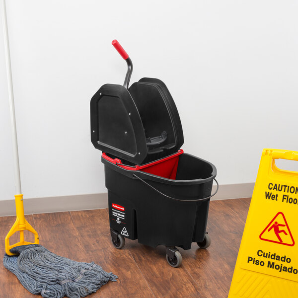 A Rubbermaid Executive Series WaveBrake mop bucket and dirty water bucket on a wood floor next to a mop stand.