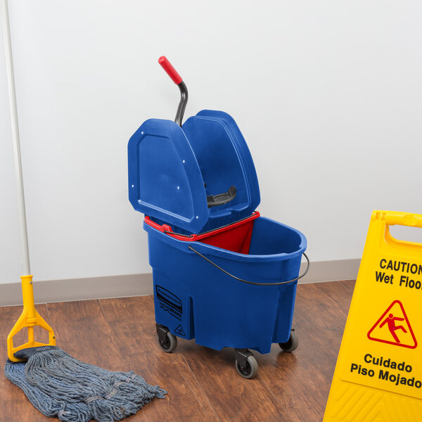 A Rubbermaid blue mop bucket with red wringer and dirty water bucket next to a mop stand.