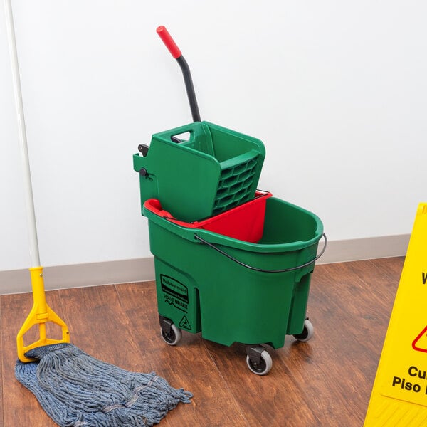A Rubbermaid green mop bucket with red dirty water bucket on a wood floor.
