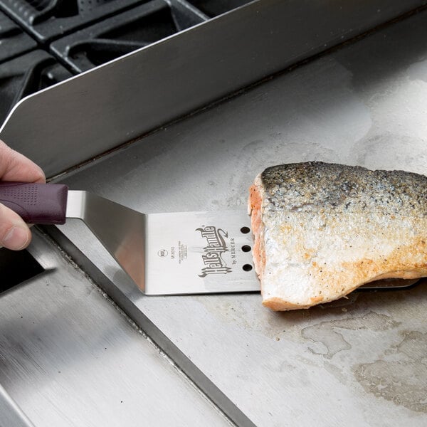 A person using a Mercer Culinary Hell's Handle Perforated Turner to serve a piece of fish.