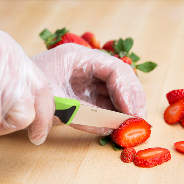A person cutting a strawberry with a Mercer Culinary Millennia paring knife with a green handle.