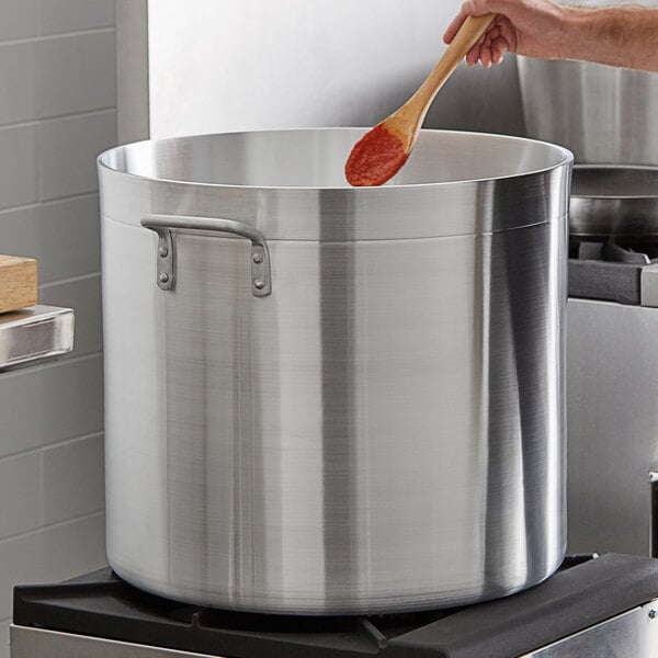 A person stirring red sauce with a wooden spoon in a large silver Choice stock pot.