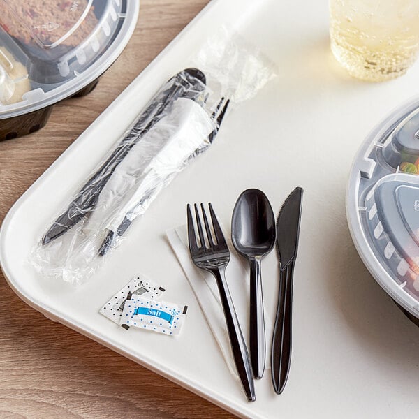 A plastic tray with wrapped black plastic cutlery on it.