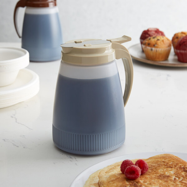A Vollrath Dripcut polyethylene server with an almond lid dispensing blue liquid onto a plate of pancakes.
