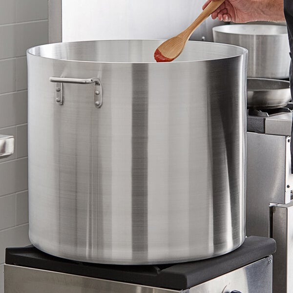 A man stirring a Choice 120 Qt. aluminum stock pot on a stove with a wooden spoon.