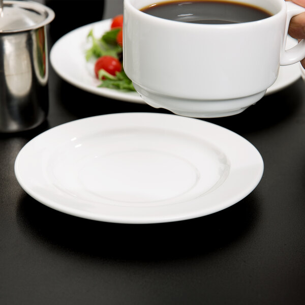 A hand holding a cup of coffee on a Arcoroc white porcelain saucer.