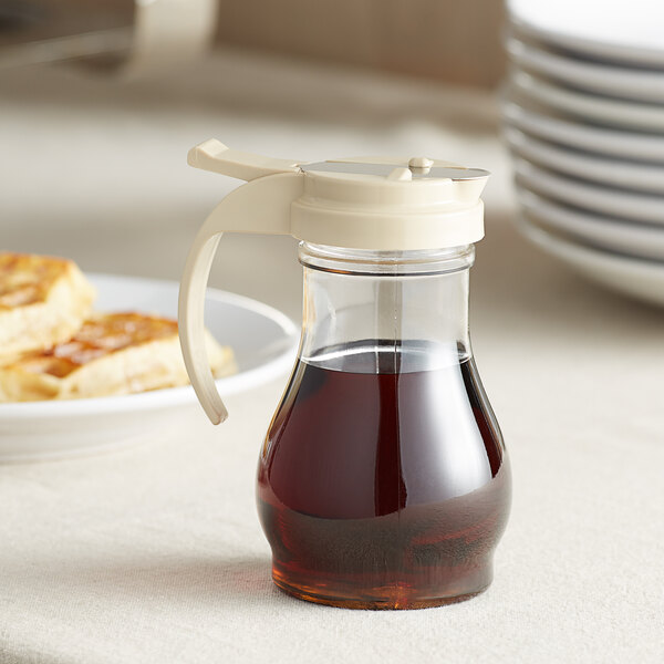 A clear polycarbonate teardrop syrup server filled with syrup on a plate.