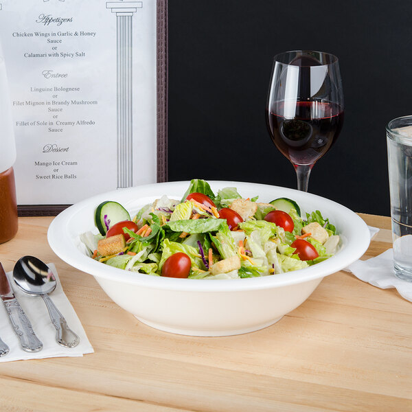 A Super Bright White porcelain serving bowl filled with salad on a table with wine glasses and a spoon.
