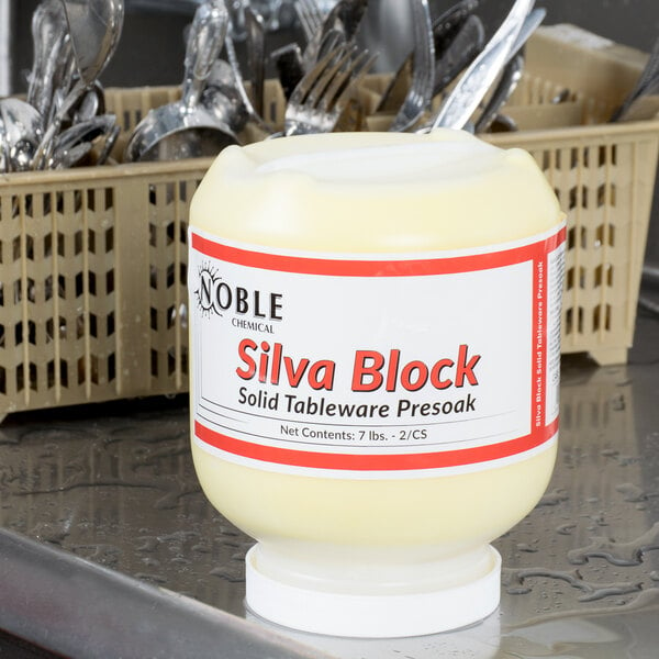A white plastic container of Noble Chemical Silva Block on a counter next to tableware.