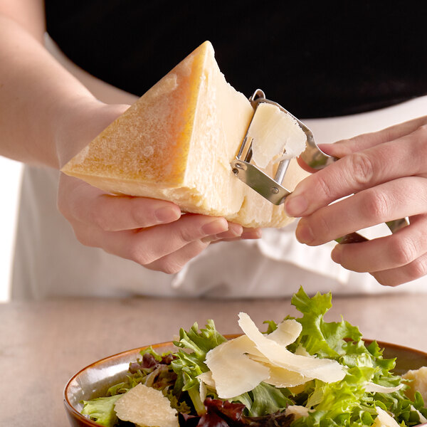 A person cutting a wedge of Agriform Grana Padano cheese on a salad.