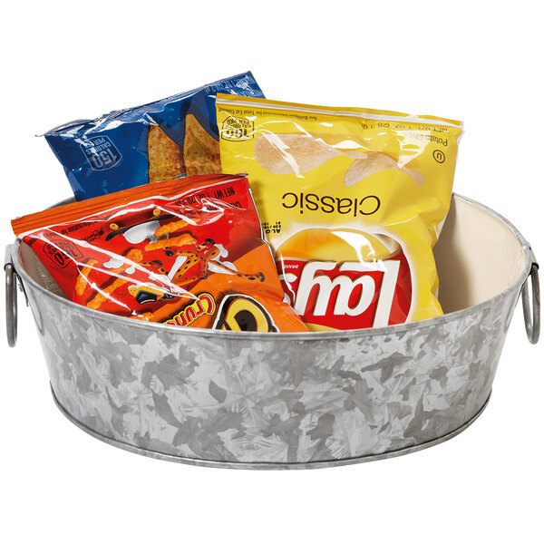 A galvanized metal tray with handles filled with bags of chips on a counter.