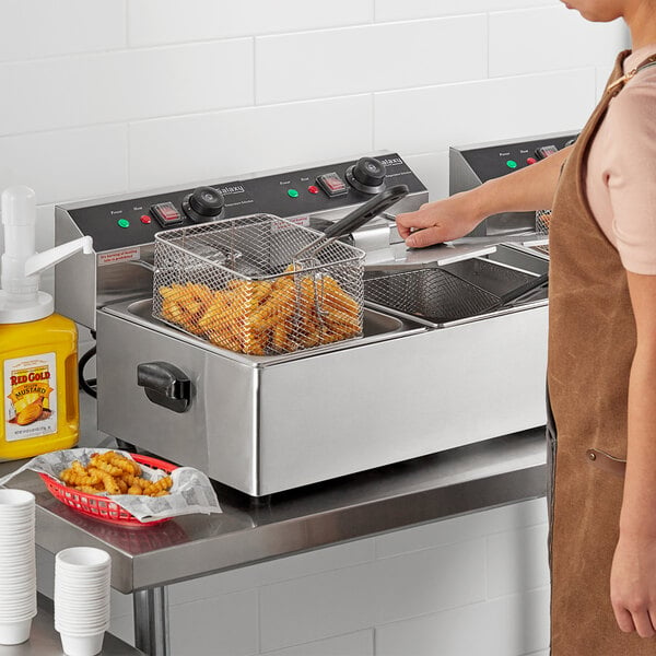 A woman using a Galaxy dual tank electric countertop fryer to cook french fries.