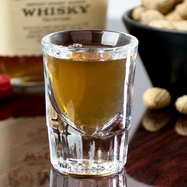 A Libbey fluted shot glass filled with brown liquid on a table.