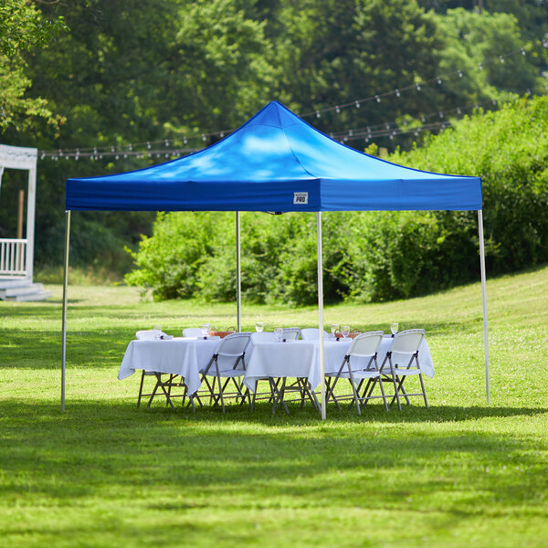 A blue Backyard Pro Courtyard Series canopy with a white table and chairs set up on a lawn.