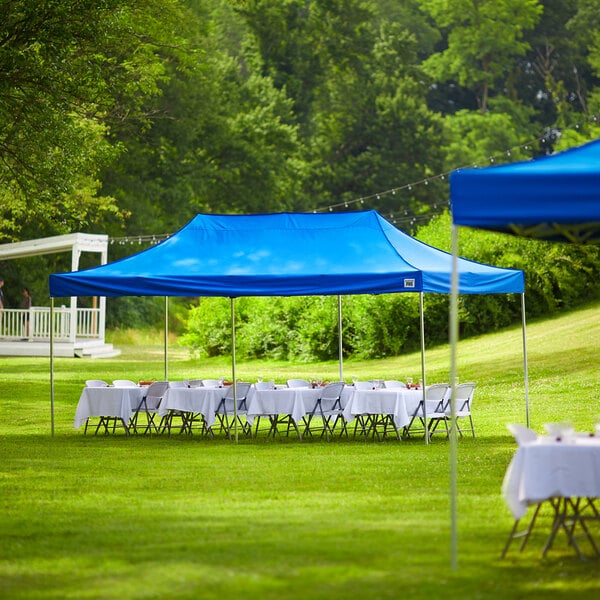 A Backyard Pro Courtyard blue canopy set up over tables with white tablecloths in a grassy area.