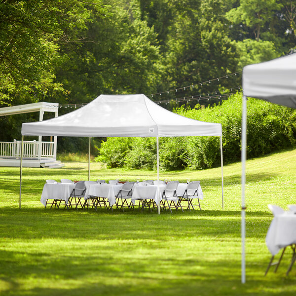 A white Backyard Pro Courtyard Series canopy set up in a grassy area with tables and chairs.