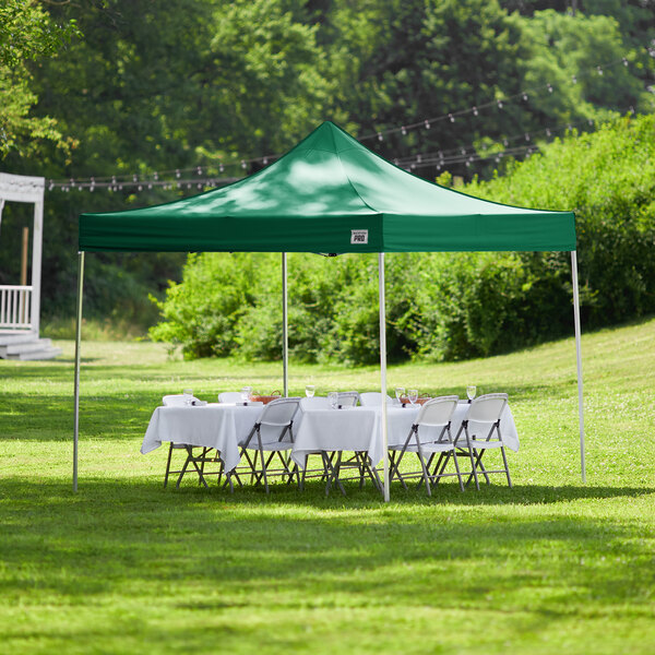 A green Backyard Pro Courtyard Series canopy set up with white table and chairs on grass.