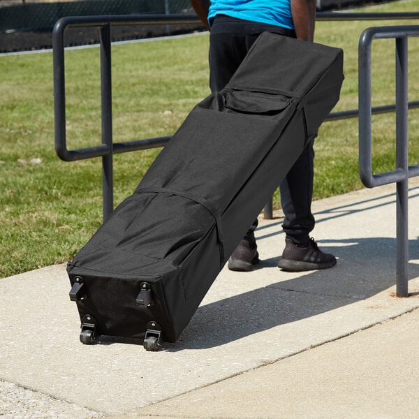 A man in a blue shirt carrying a black Backyard Pro Courtyard Series Canopy roller bag.